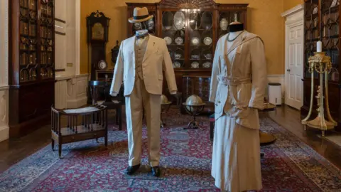 Andy Dunkley A man's linen suit with straw Panama hat and a woman's cream linen and silk skirt and jacket - both in a 1930s style