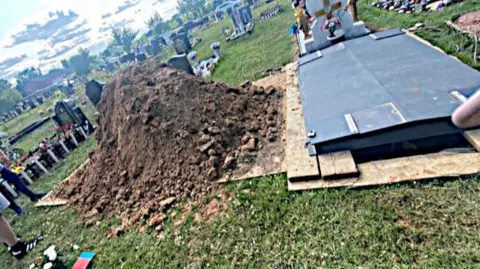 On the left is a pile of earth, covering the grave of Christopher Cooper. That earth has been dug to create a new grave on the right hand side of the picture. 