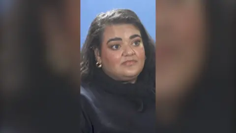 Billie Bhatia has long dark hair and is wearing a dark top.