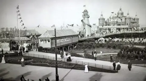 Great Yarmouth Borough Council Old black and white photo of Great Yarmouth Britannia Pier, showing a buzz of activity including a helter skelter, the pier building and hundreds of people enjoying the sun