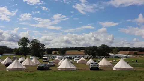 Nene Valley Rock Festival A field under a blue sky, with about a dozen white glamping pods.