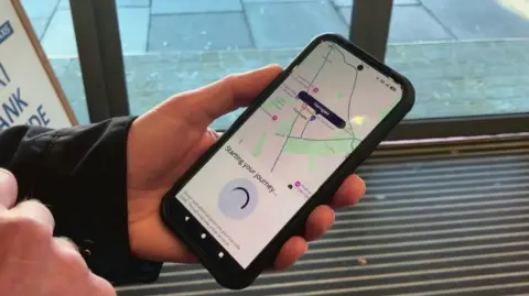 A phone displays the pay-as-you-go app, which tracks the user at Harrogate station.