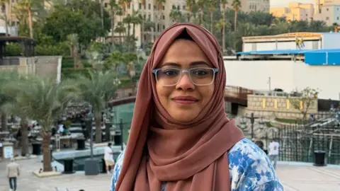 Handout Afsha Farooqui smiles at the camera. She has a brown headscarf on and glasses.