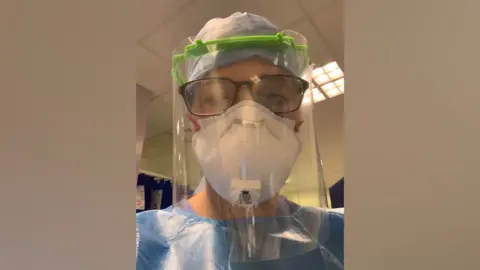 Lauren Jake Senior Sister Lauren Jake at Full PPE during the second wave of Kovid epidemic in 2021. She is wearing a gown, hair net, FFP3 mask and a full face visual. 