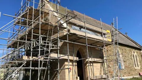 Scott Dalton / BBC the church with lots of scaffolding on it on a sunny day - you can see lots of clean sandstone contrasting with the old brick showing where the repairs have been made