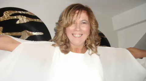 Family A woman dressed in white with curly brown hair is smiling at the camera.