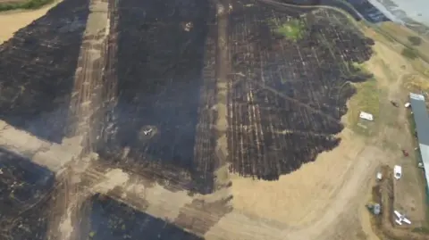 A drone shot showing charred grasslands near runways at an airstrip. A small  plane is parked on the right.