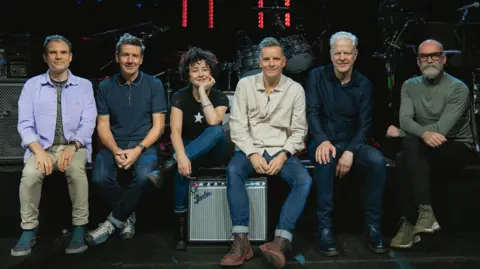 Jamie Carter The six Deacon Blue members sitting near a stage, smiling for a picture.
