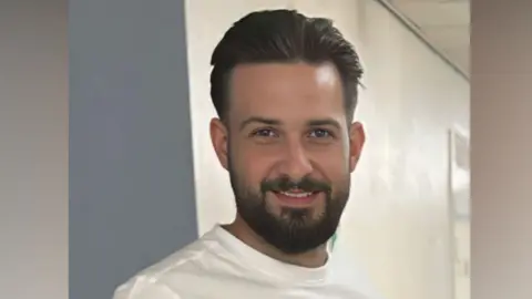 Ryan Scarth died in a crash on the A1(M) near Durham. He has short but thick black hair combed back, a trimmed beard and green eyes. He is wearing a white t-shirt and smiling at the camera.