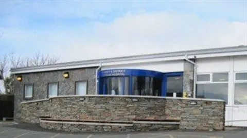 IOM GOVERNMENT The front entrance to the hospital, which it ones-storey and has a blue revolving door.