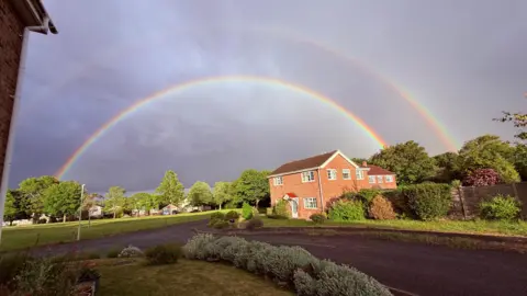 Les51 A rainbow arching over houses with a road and park visible in this residential but very green area.