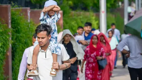 Getty Images Visitors seen using umbrellas to protect themselves from sun on hot summer day outside Lotus temple, on April 17, 2026 in New Delhi, India.