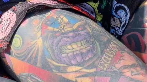 Simon Spark / BBC Close up of the Thanos tattoo who has a purple face and blue helmet 