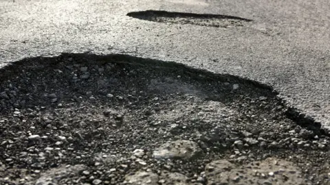 A close-up image of a road with two large potholes. 