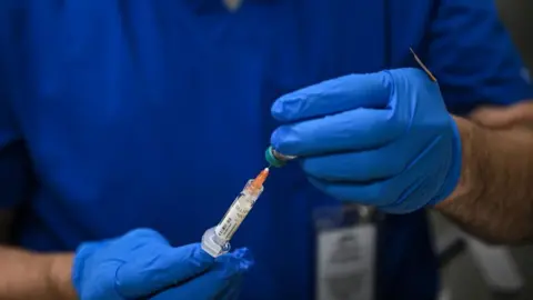 File image of a pair of hands carrying a syringe filled with measles vaccine