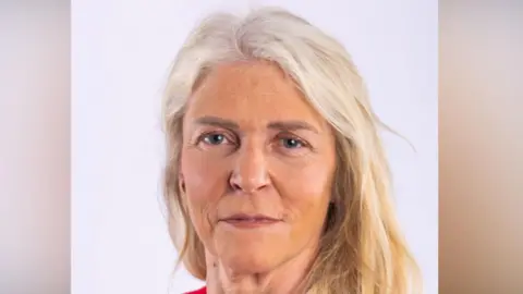 Lisa has long blonde hair and is smiling at the camera in this head and shoulders image. She has a red top on.