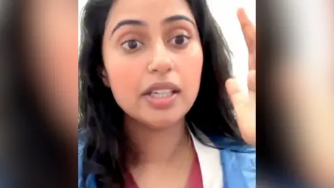 A woman with long, dark hair talks to the camera