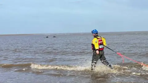 A coastguard officer is tied to a safety rope as he wades out to rescue the stranded walkers.