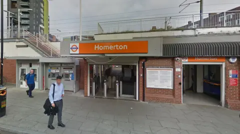 Homerton station entrance shows orange London Overground signage and two men to the left 