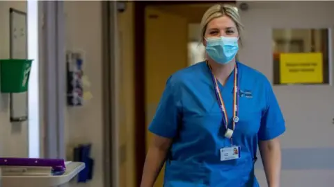 Getty Images A NHS staff member walking down a corridor wearing a mask and blue scrubs