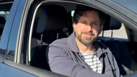 Gareth Wild sitting in the driver seat of his car. He is looking at the camera.