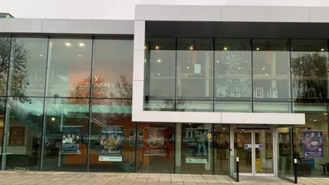 The exterior of the theatre, which is a grey building with a glass front.