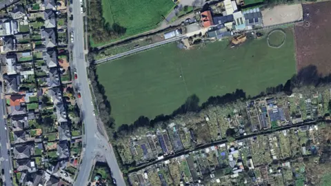 An aerial view over Flass Lane in Barrow. There is a large patch of green grassy land off Flass Lane which is among dozens of residential houses with gardens. 