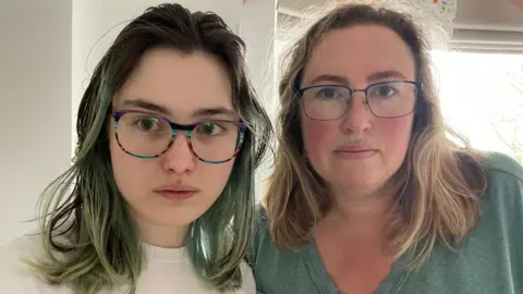 Supplied A teenage girl and a woman in her 40s, both wearing glasses, look to the camera with neutral expressions. The girl has dyed green hair and wears a white t-shirt, and the woman has light brown hair and wears a teal t-shirt.