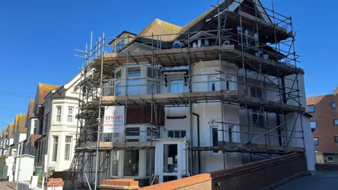 George Carden/BBC The former hotel building where the club operates is a three-storey cream coloured building which is covered in scaffolding. It is in a residential area houses all down the road near the seafront