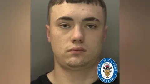 West Midlands Police A mugshot of a man with short brown hair, facial stubble in the shape of a goatee and a slit through his eyebrow. He is wearing a black T-shirt.