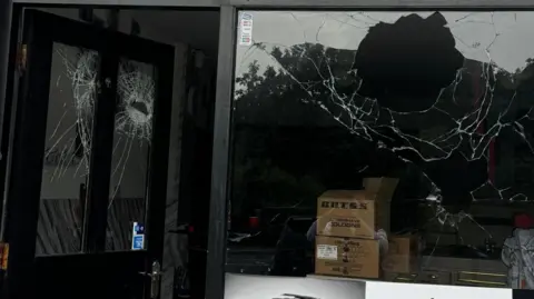 Skin Fade Syrian Barbers A front window of the barber shop has two large holes with smashed glass.
A door with two window panes is also damaged in two places