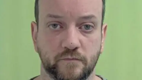 IOM CONSTUABLRY Police mugshot of Scott Goulden, who has short dark hair and a short beard. The background is green.