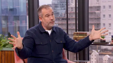 A man in a blue shirt spreads his hands out infront of him