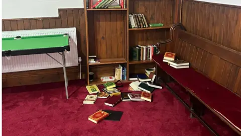 Ben Pickering Books of religious texts are scattered on a room's red-carpeted floor.