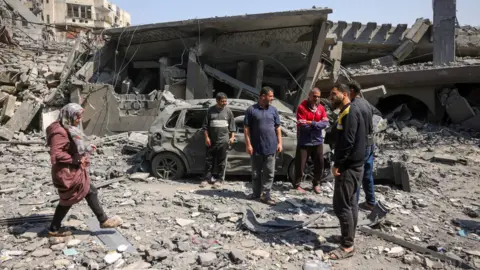 People walk amid the rubble of a building destroyed in an overnight Israeli strike in Jabalia on 18 March.