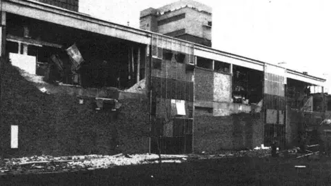 HMSO A black and white image of one of the GF buildings with large holes in it, caused by the explosion.