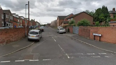 An image of a residential street with cars parked on either side of the road.