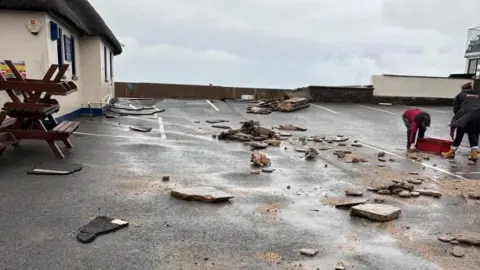 People are seen cleaning up a car park after debris are strewn over the road.
