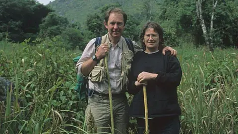 Bleddyn and Sue Wynn Jones Bleddyn and Sue Wynn Jones in tall grass with trees and mountains in the background