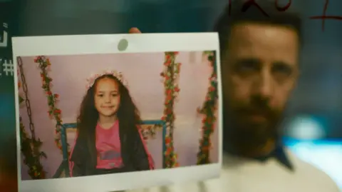 Actor Motaz Malhees places a photo of Hind Rajab on a glass wall