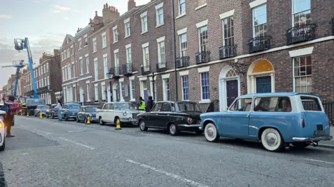 Cara D Photography Classic cars typical of the late 1950s and early 1960s are parked on the road in front of terraced houses
