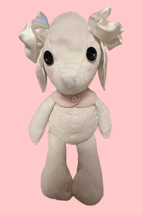 Fi Austin A picture of a very delicate looking teddy bear bunny. It is mostly white with a a few pink elements. It has black button eyes and white wedding dress bows above its ears.