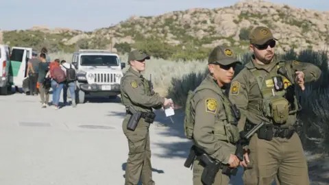 Getty Images Migrants being detained by US border patrol officers in California. 