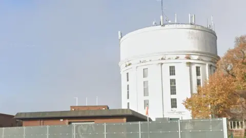 A white cylindrical building behind metal fencing