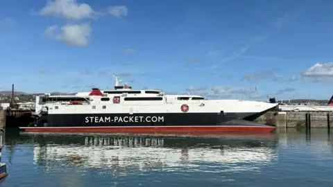 A closeup of the Manannan in the sunshine at Douglas Harbour, the sleek catamaran is white, navy and red withh writing that reads Steam Packet.