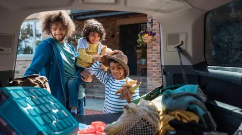 Getty Images A dad and his two children packing a car with luggage