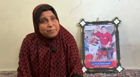 Majdiya stares down the camera, with a photo of Ahmed in the background. 