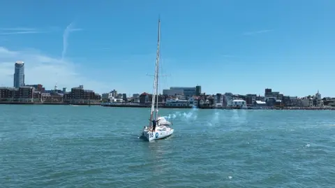 Sean Herbert, Premier Marinas James Ketchell returns to Gosport on a sunny day. His hands are in the air. The town is behind him.