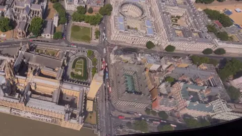 Aerial view from a blimp over Westminster in central London, showing the Palace of Westminster, Westminster Abbey and surrounding streets beside the River Thames.