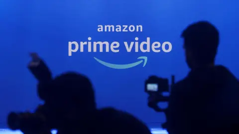 the Amazon Prime Video logo projected on a screen as photographers in shadow aim their cameras.